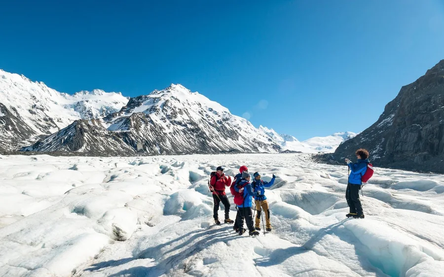 Hikers roped up on the ice of the Tasman Glacier with Aoraki behind